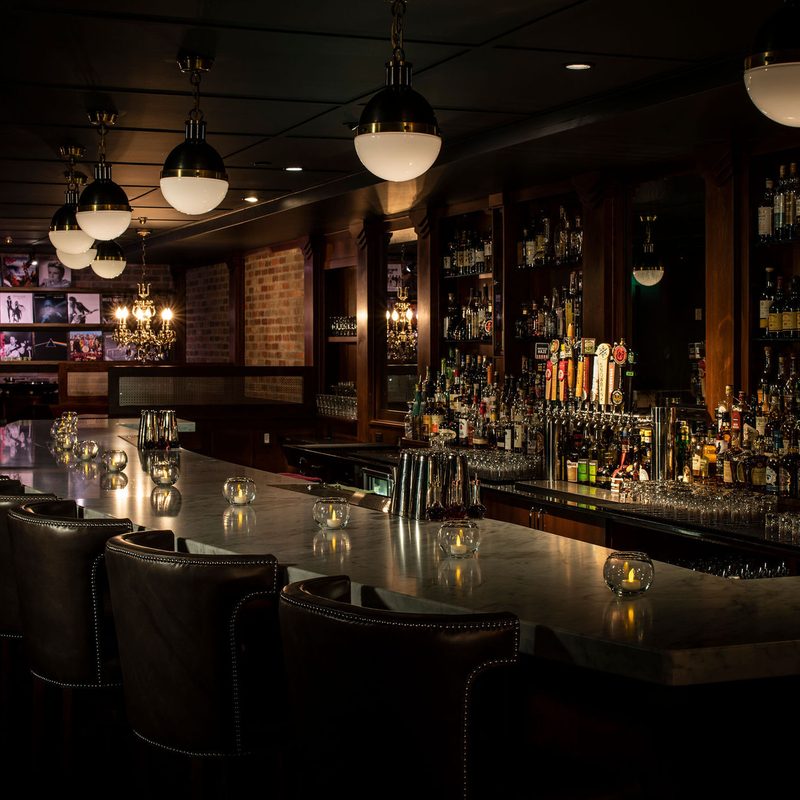 Underground marble bar with leather chairs and pendant lights against a deep liquor wall