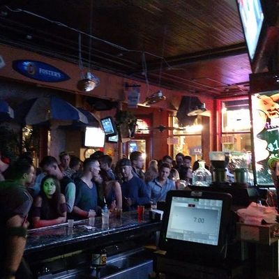 Packed bar at night with a crowd lined up under TVs and a disco ball