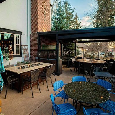 Busy side patio under blue-striped umbrellas with people drinking wine at wooden tables