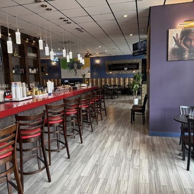 Long red-topped bar with red leather stools, pendant lights, and Indian-inflected artwork on purple walls