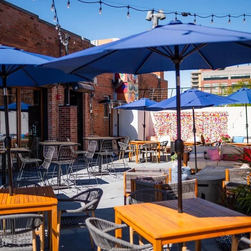 Rooftop with blue umbrellas, wooden tables, and string lights overlooking downtown Fort Collins