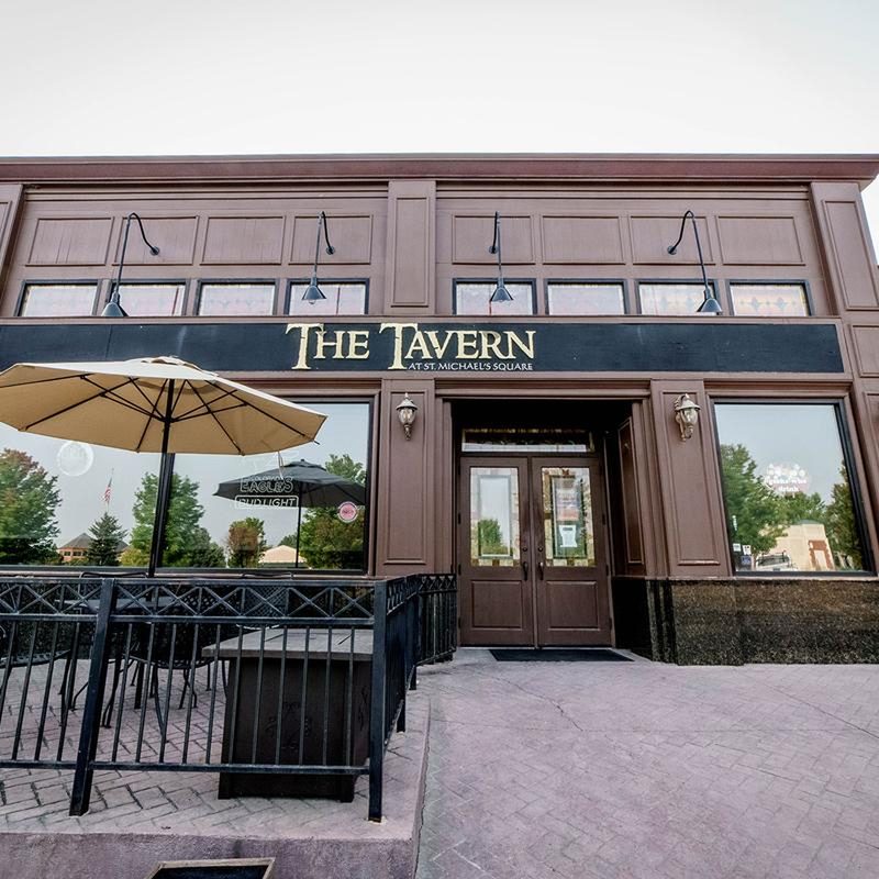 Two-story wood-paneled exterior with a railed front patio and tan umbrella under 'The Tavern' sign