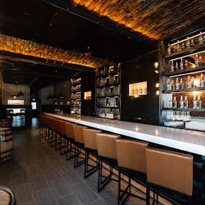 Twin Staves marble bar lined with leather stools beneath a lit whiskey wall.